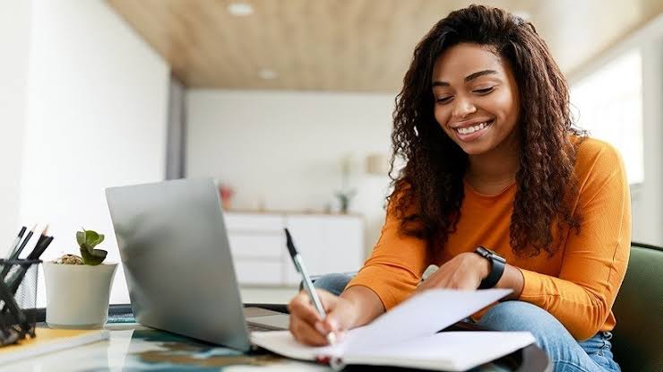 Black woman smiling while studying with a laptop and notebook, representing online learning—highlighting why TechVerve is unique for online tech education