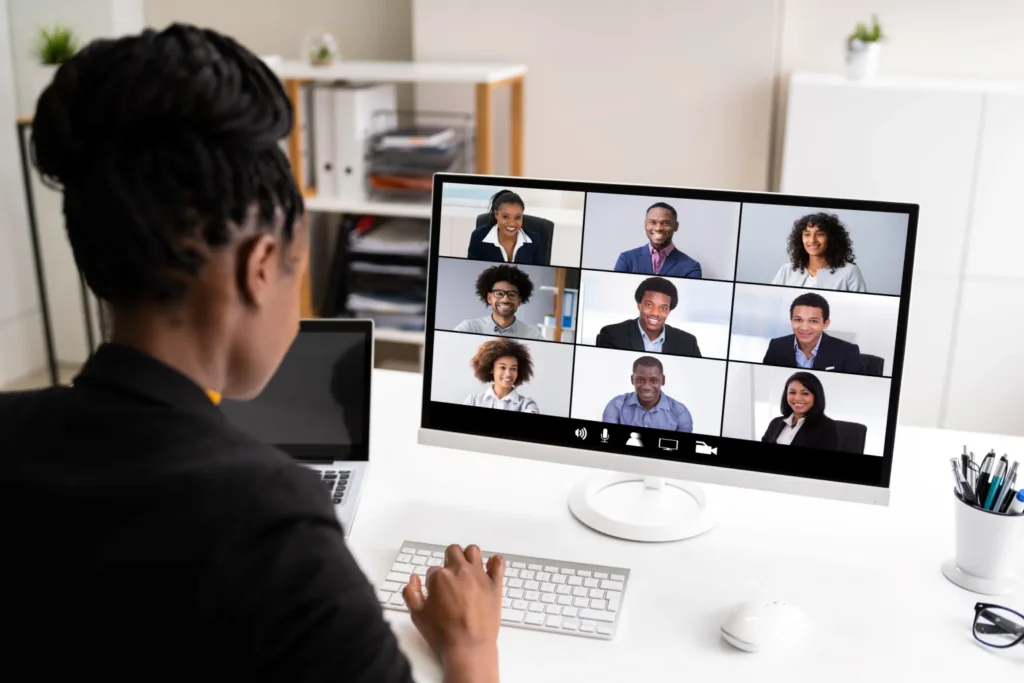 Black woman attending a virtual tech meeting on her desktop with her team, showcasing remote collaboration and online learning.